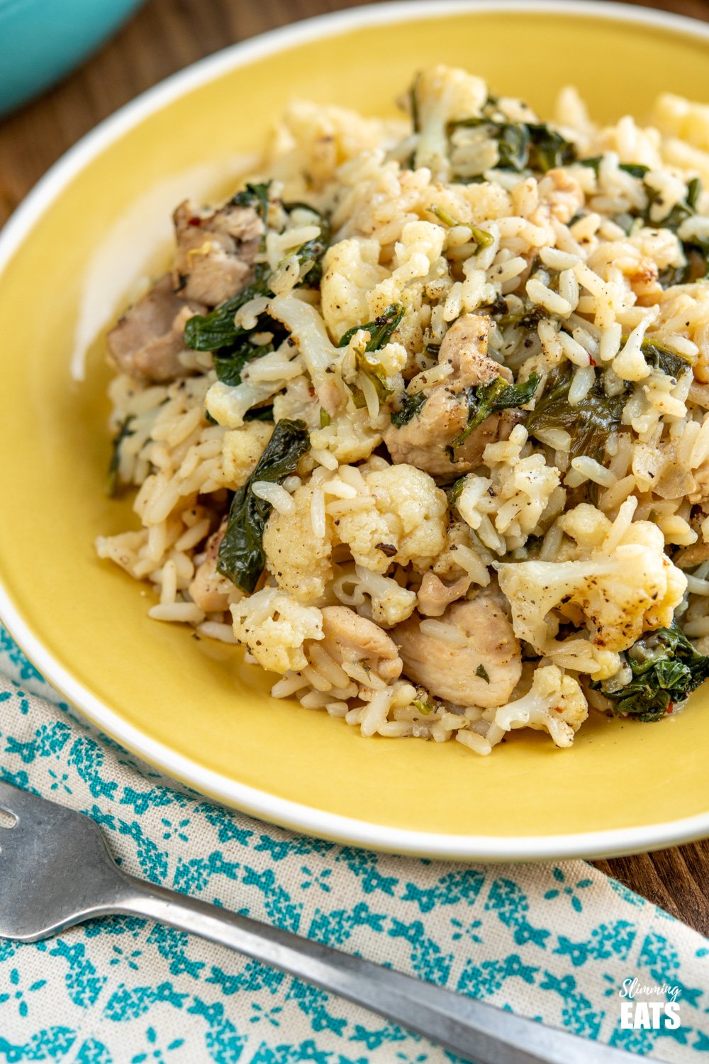 One Pot Lemon Garlic Chicken Rice - a simple all in one pan recipe with the delicious flavours of lemon and garlic and packed with healthy vegetables such as cauliflower and spinach. Dairy free, gluten free. close up of yellow plate of one pot lemon garlic chicken rice with fork to side
