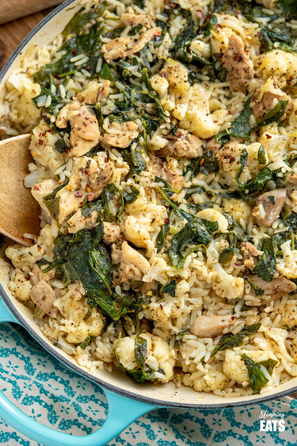 One Pot Lemon Garlic Chicken Rice - a simple all in one pan recipe with the delicious flavours of lemon and garlic and packed with healthy vegetables such as cauliflower and spinach. Dairy free, gluten free. close up of one pot lemon garlic chicken rice in cast iron casserole pan with wooden spoon