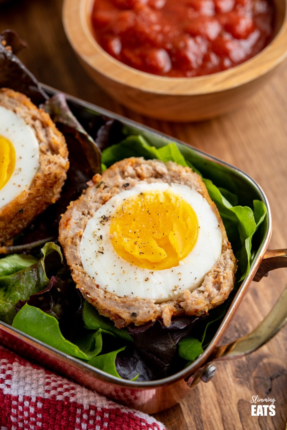 close up Oven Baked Scotch Egg in a small metal tray lined with baby salad leaves served with relish