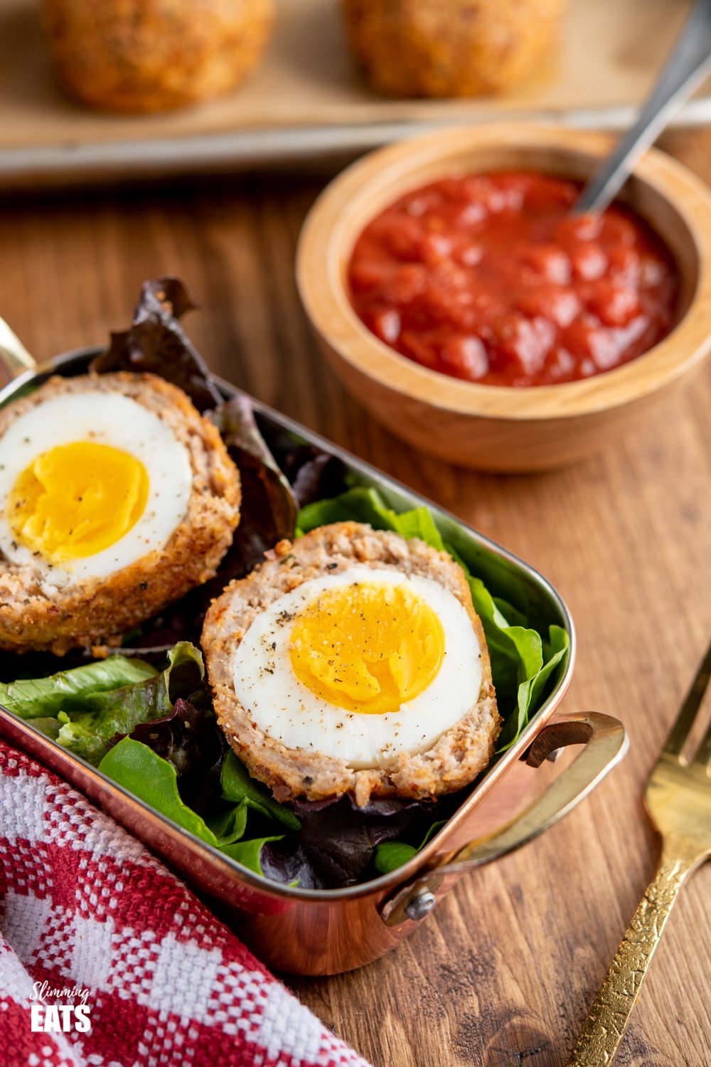 Oven Baked Scotch Egg in a small metal tray lined with baby salad leaves served with relish