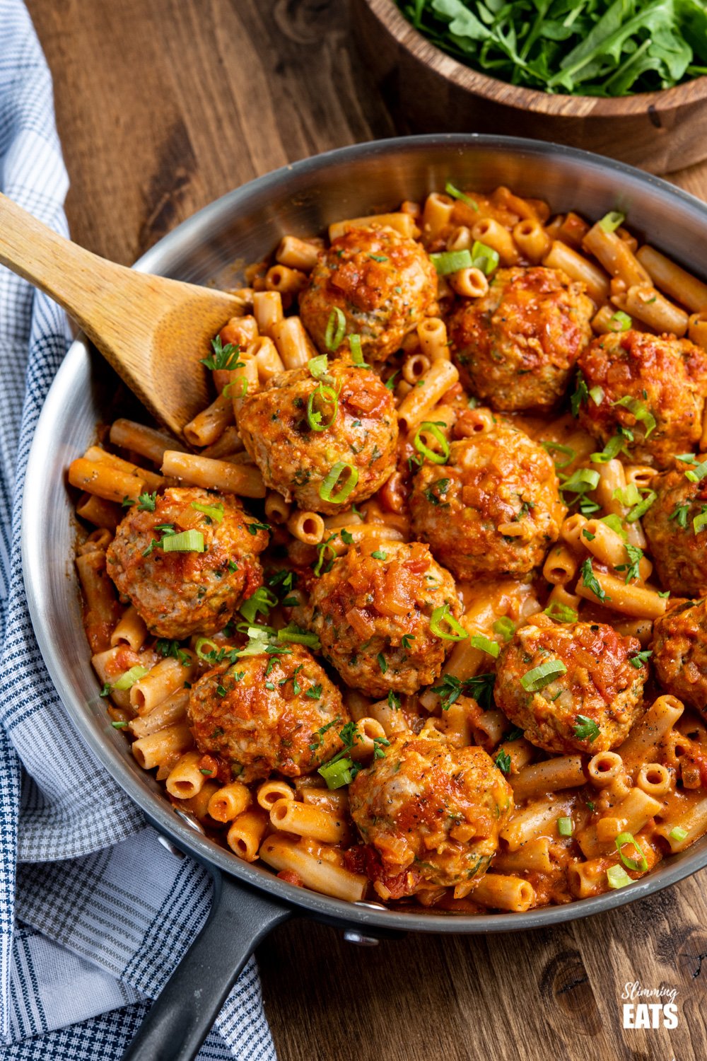 creamy cajun meatballs pasta with dairy free sauce and gluten free pasta in frying pan with wooden spoon, bowl of arugula in background