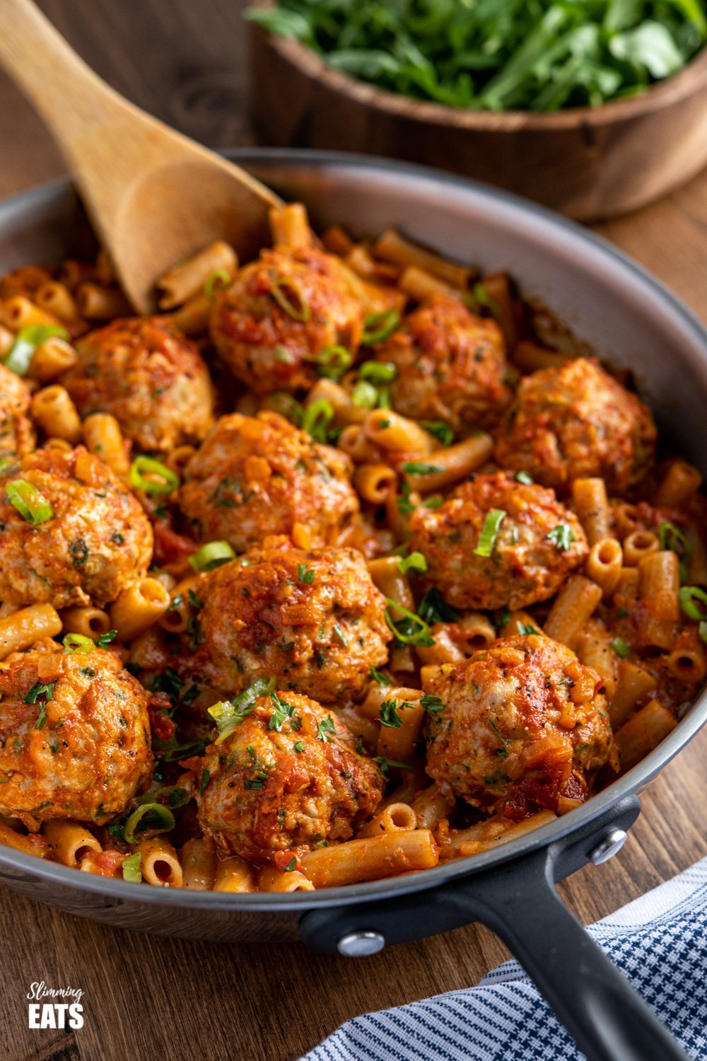 creamy cajun meatballs pasta in frying pan with wooden spoon