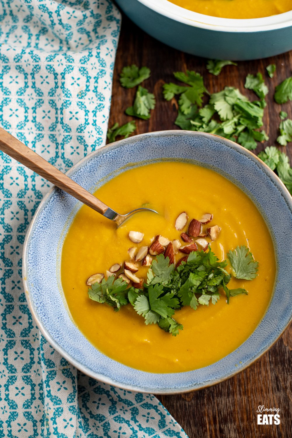 over the top view of ginger carrot cauliflower soup in blue bowl topped with coriander and almonds