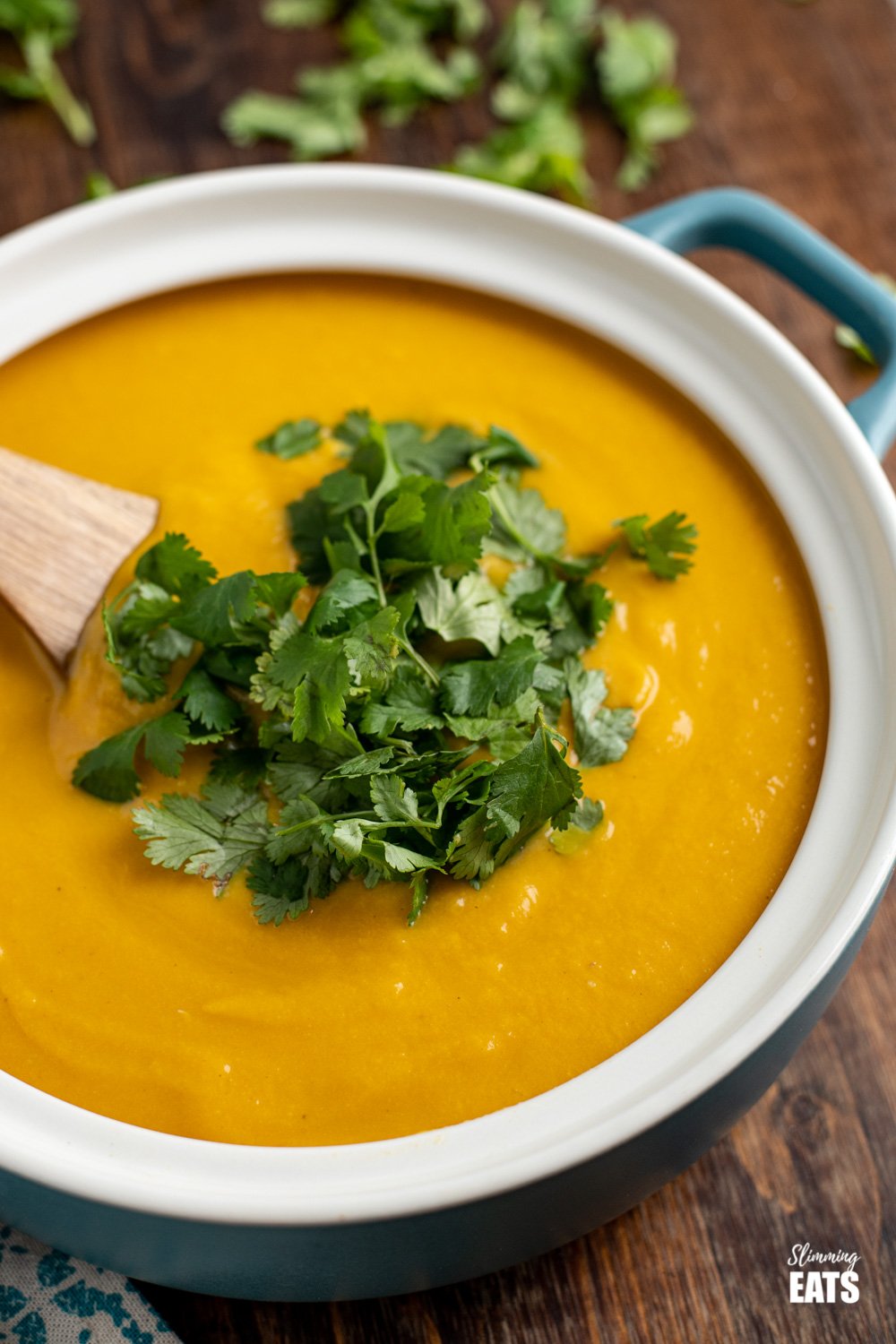 close up of ginger carrot cauliflower soup in blue gray soup pan topped with coriander