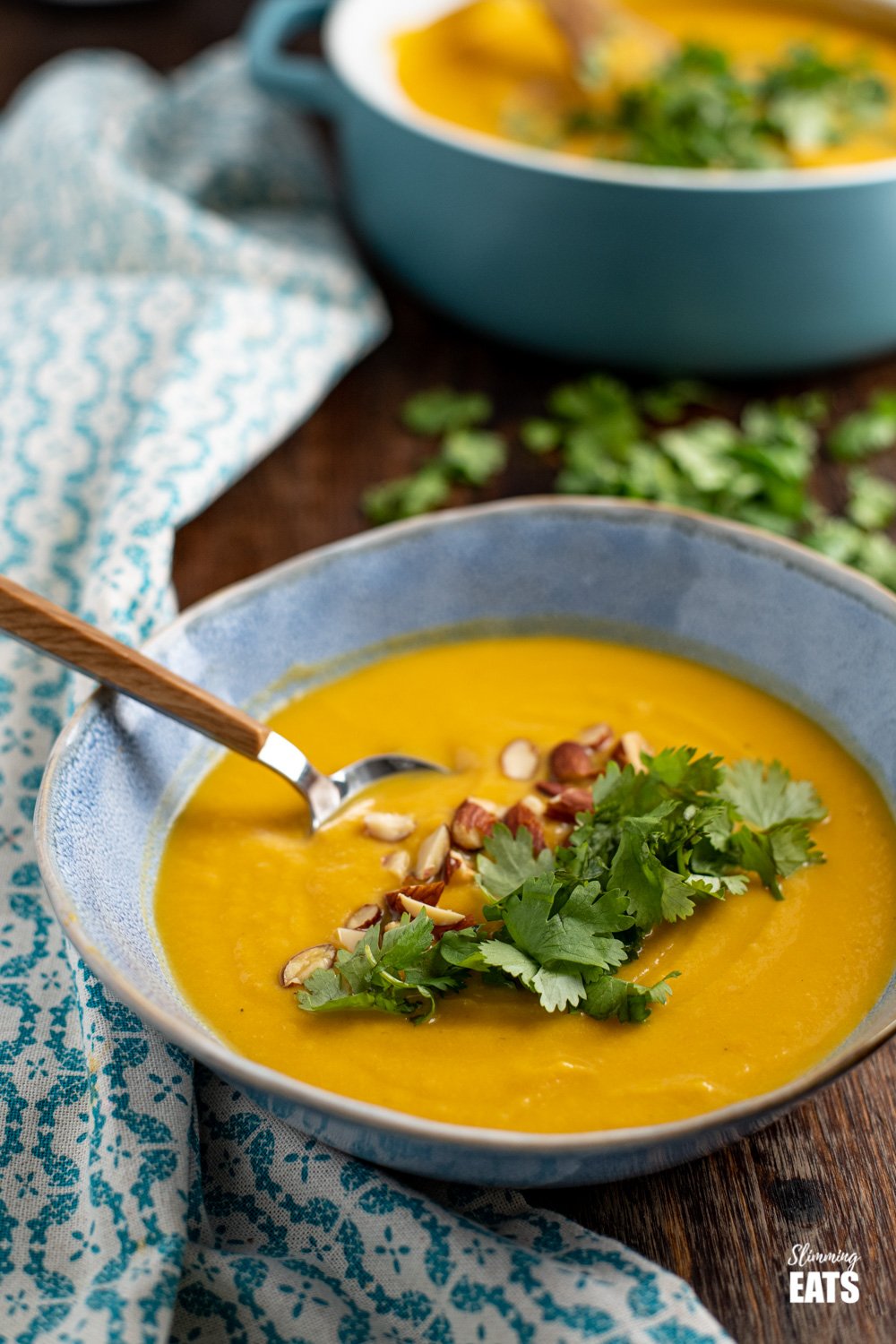 wooden handles spoon in bowl of ginger carrot cauliflower soup next to patterned napkin on wooden board