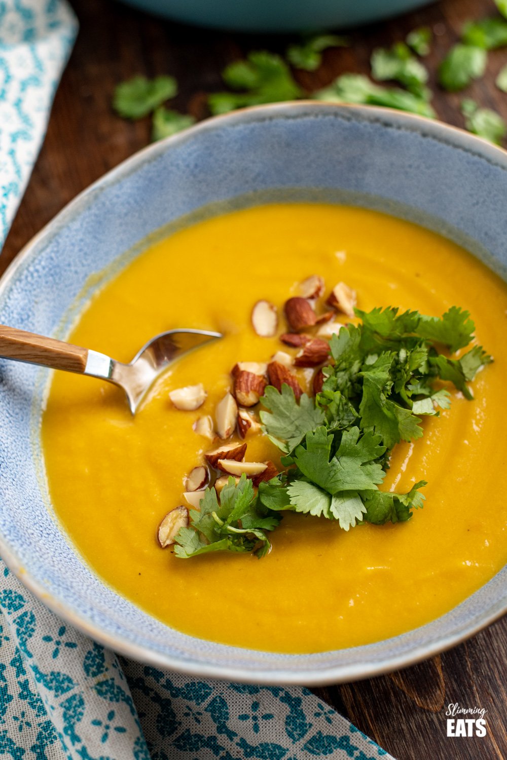 close up of ginger cauliflower carrot soup in blue bowl topped with chopped almonds and coriander