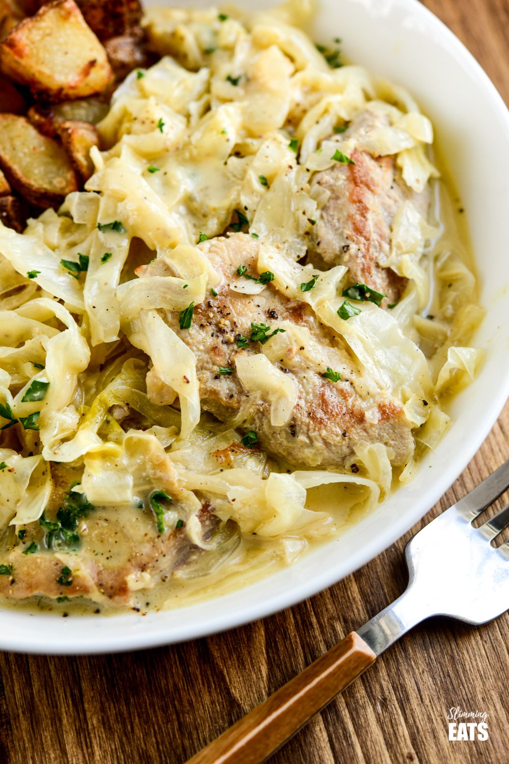 close up of creamy garlic pork with cabbage in white dish with fork to side. 