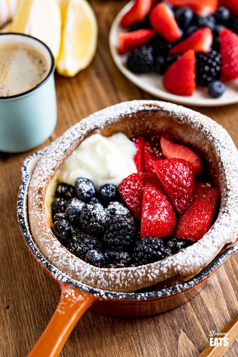 Healthier Dutch Baby with Berries and Yoghurt dusted with icing sugar in cast iron skillet