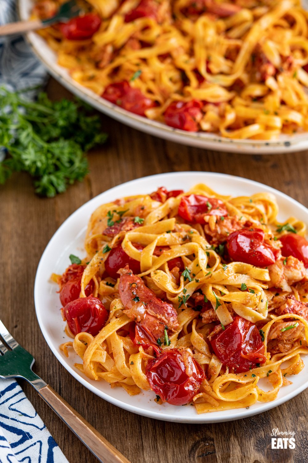 serving of lobster pasta with tagliatelle pasta on a white plate with fork to the left. 