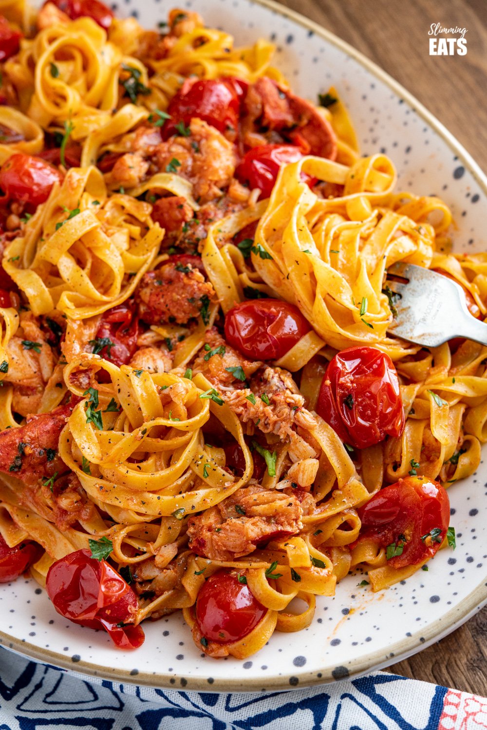 fork spiralling up tagliatelle from speckled oval plate filled with lobster pasta