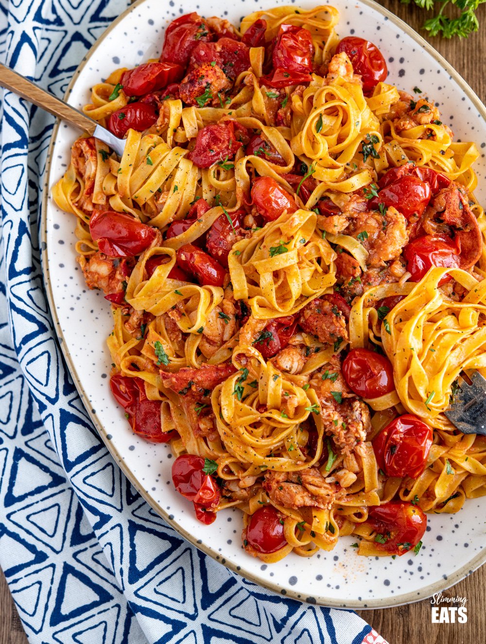 The most amazing fresh Lobster Pasta with the delicious sweet taste of fresh tomatoes and a lemon parsley buttery sauce. et taste of fresh tomatoes and a lemony garlic buttery sauce. Slimming Eats and Weight Watchers friendly Lobster Pasta on a large oval speckled dish with two forks spiralling the tagliatelle