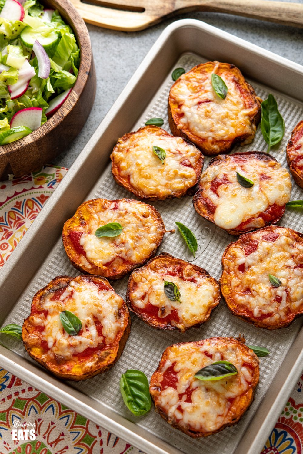 Delicious Cheesy Air Fryer Pizza Sweet Potato Slices - because all the pizza lovers out there should turn everything into Pizza. Gluten Free, vegetarian, Slimming Eats and Weight Watchers friendly air fryer pizza sweet potato slices on a baking tray with scattered fresh basil and bowl of salad to the left