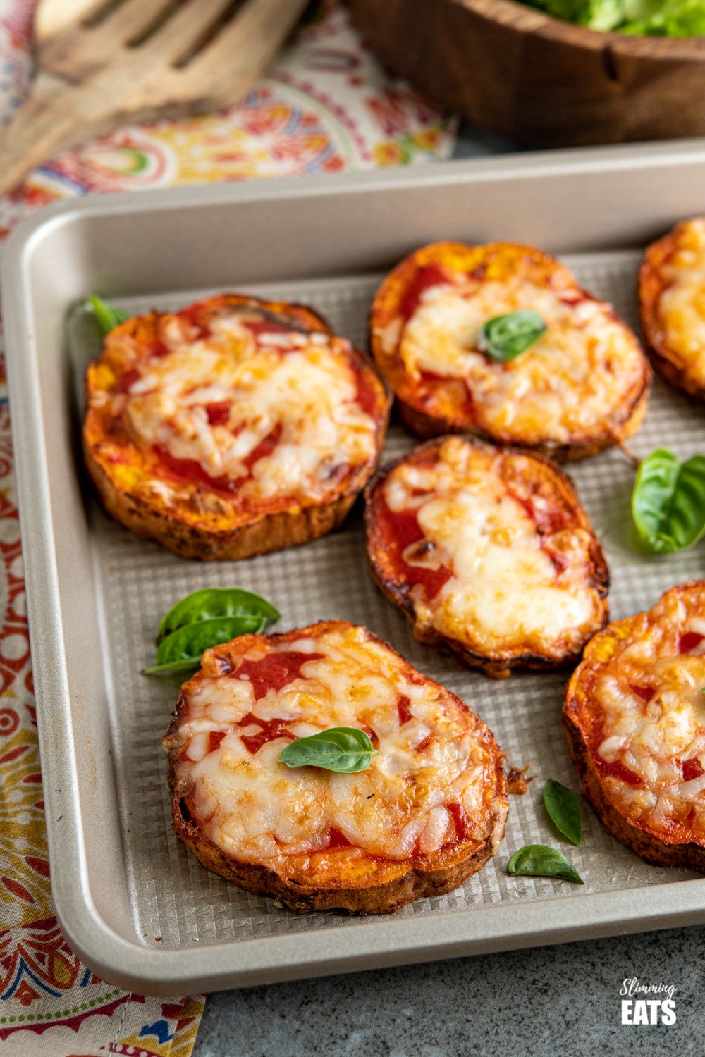 Delicious Cheesy Air Fryer Pizza Sweet Potato Slices - because all the pizza lovers out there should turn everything into Pizza. Gluten Free, vegetarian, Slimming Eats and Weight Watchers friendly pizza sweet potato slices on baking tray on patterned napkin with bowl of salad and spatula in background