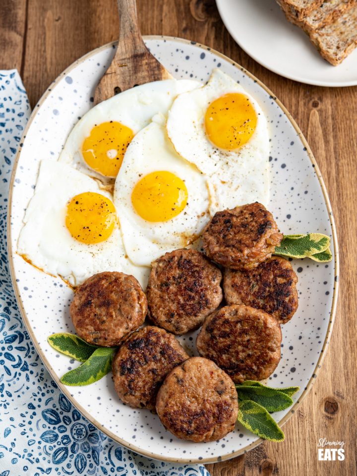 oval speckled plate filled with homemade turkey breakfast sausage patties and fried eggs, plate of wholemeal bread in the background