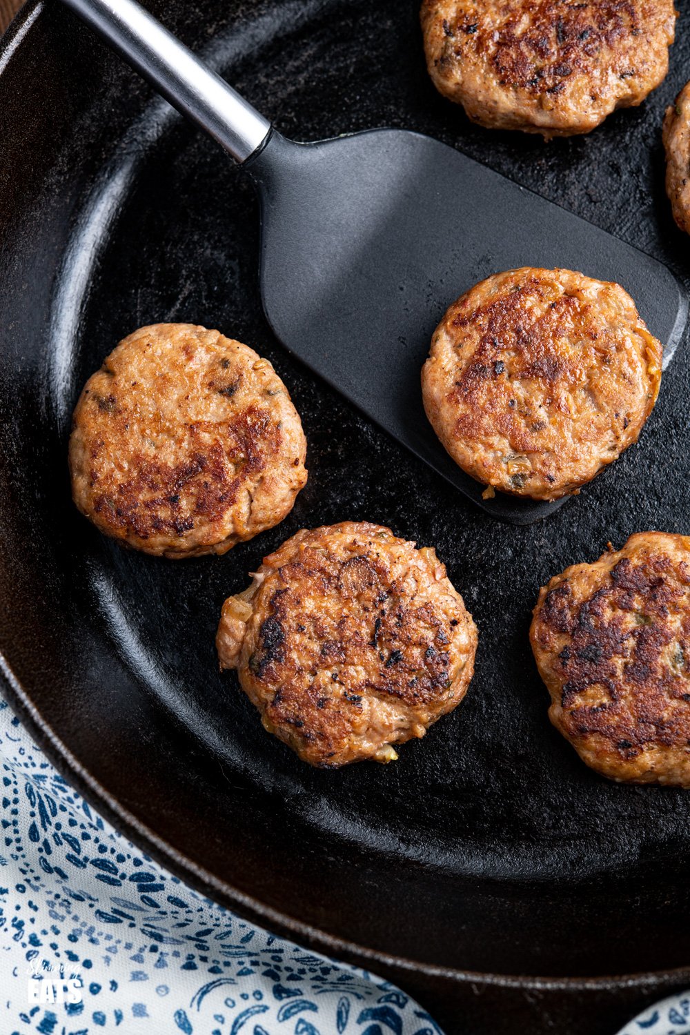 close up of cooked Turkey Breakfast Sausage Patties in a lodge cast iron skillet on spatula 