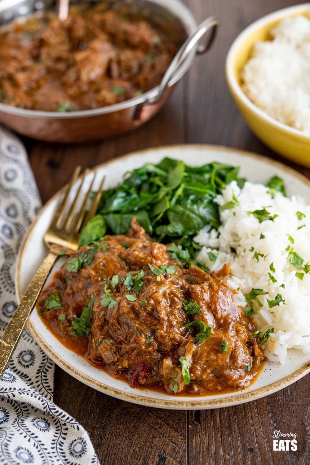 lamb bhuna on beige and white plate with rice, spinach and sprinkled with coriander