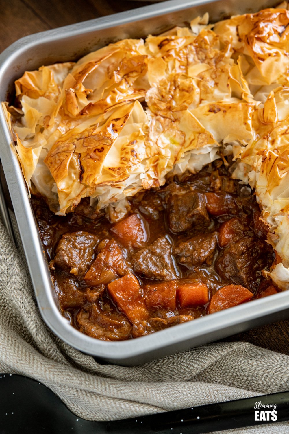 Epic Steak and Vegetable Pie with a delicious golden filo pastry topping - tender pieces of beef with carrots and onion in a deliciously rich homemade gravy. #slimmingeats #weightwatchers #dairyfree #pie #steak #filopastry #beef close up of Steak and Vegetable Pie in baking tin