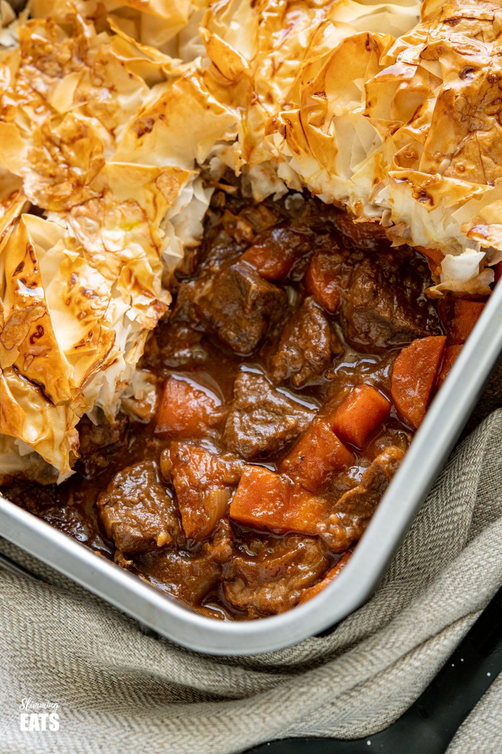 Epic Steak and Vegetable Pie with a delicious golden filo pastry topping - tender pieces of beef with carrots and onion in a deliciously rich homemade gravy. #slimmingeats #weightwatchers #dairyfree #pie #steak #filopastry #beef close up of Steak and Vegetable Pie in baking tin