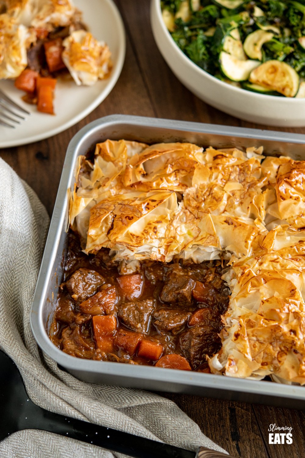 Steak and Vegetable Pie in baking tin with bowl of green vegetables in background