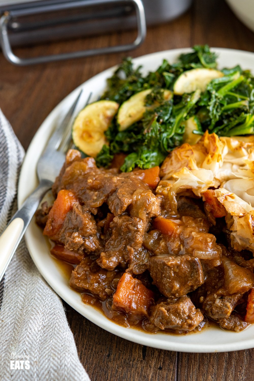 Epic Steak and Vegetable Pie with a delicious golden filo pastry topping - tender pieces of beef with carrots and onion in a deliciously rich homemade gravy. #slimmingeats #weightwatchers #dairyfree #pie #steak #filopastry #beef close up of Steak and Vegetable Pie on plate with zucchini and kale