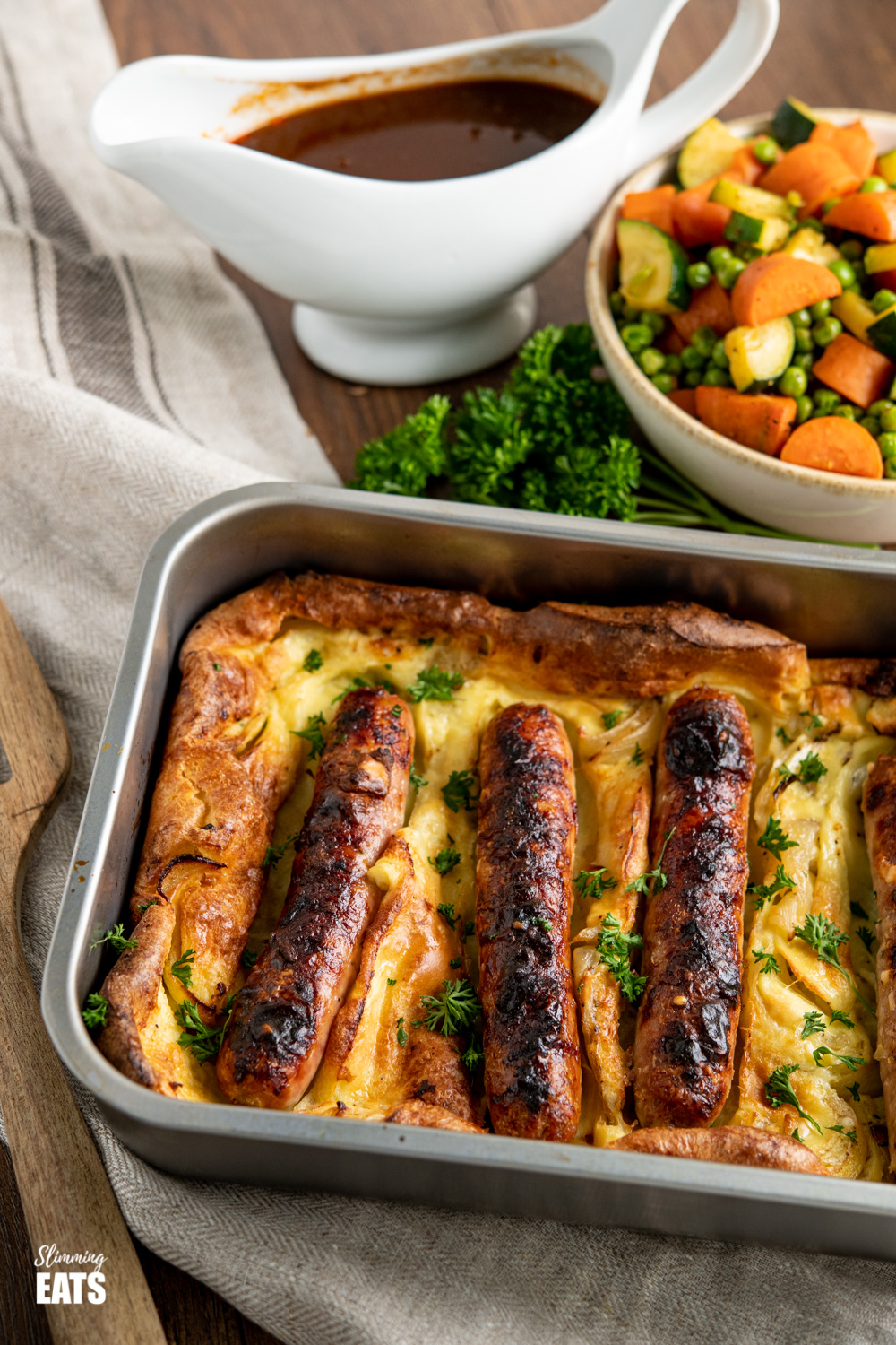 toad in the hole in baking dish with gravy and vegetables in background