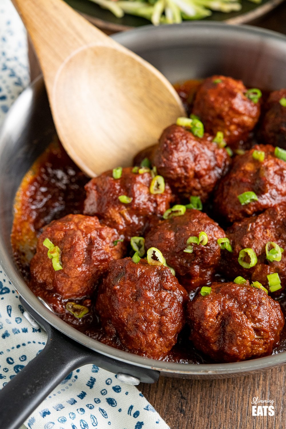 close up of honey and garlic chicken meatballs in a stainless steel frying pan with wooden spoon