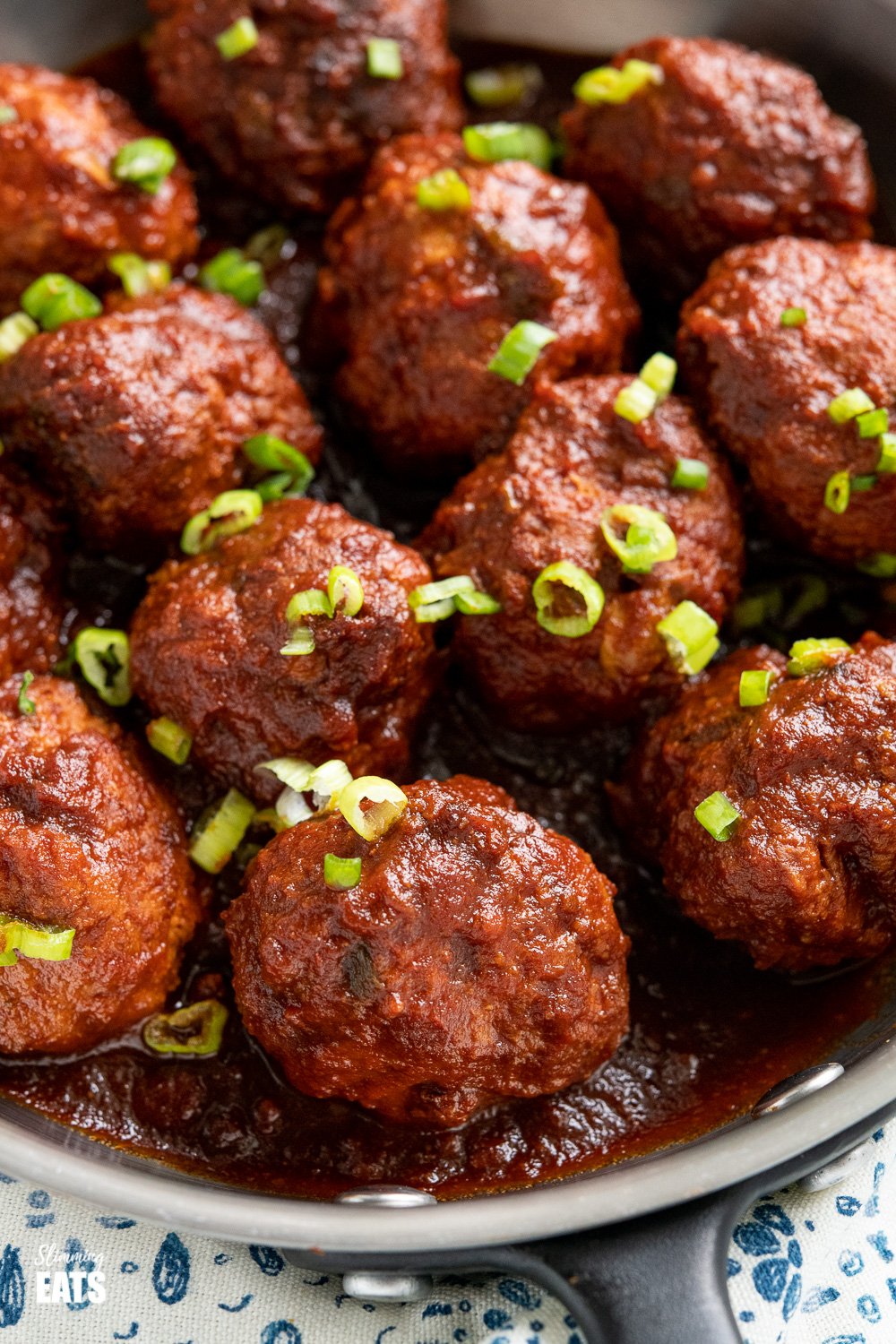 close up of honey and garlic meatballs with sauce in pan sprinkled with chopped spring onions