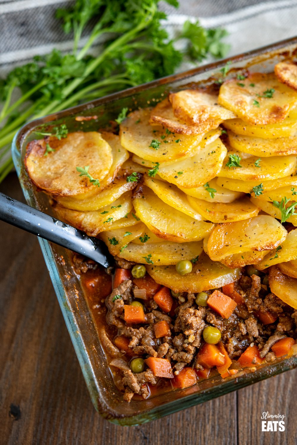 crispy potato topped meat pie (minced beef hotpot) in glass oven proof dish on wooden board with parsley