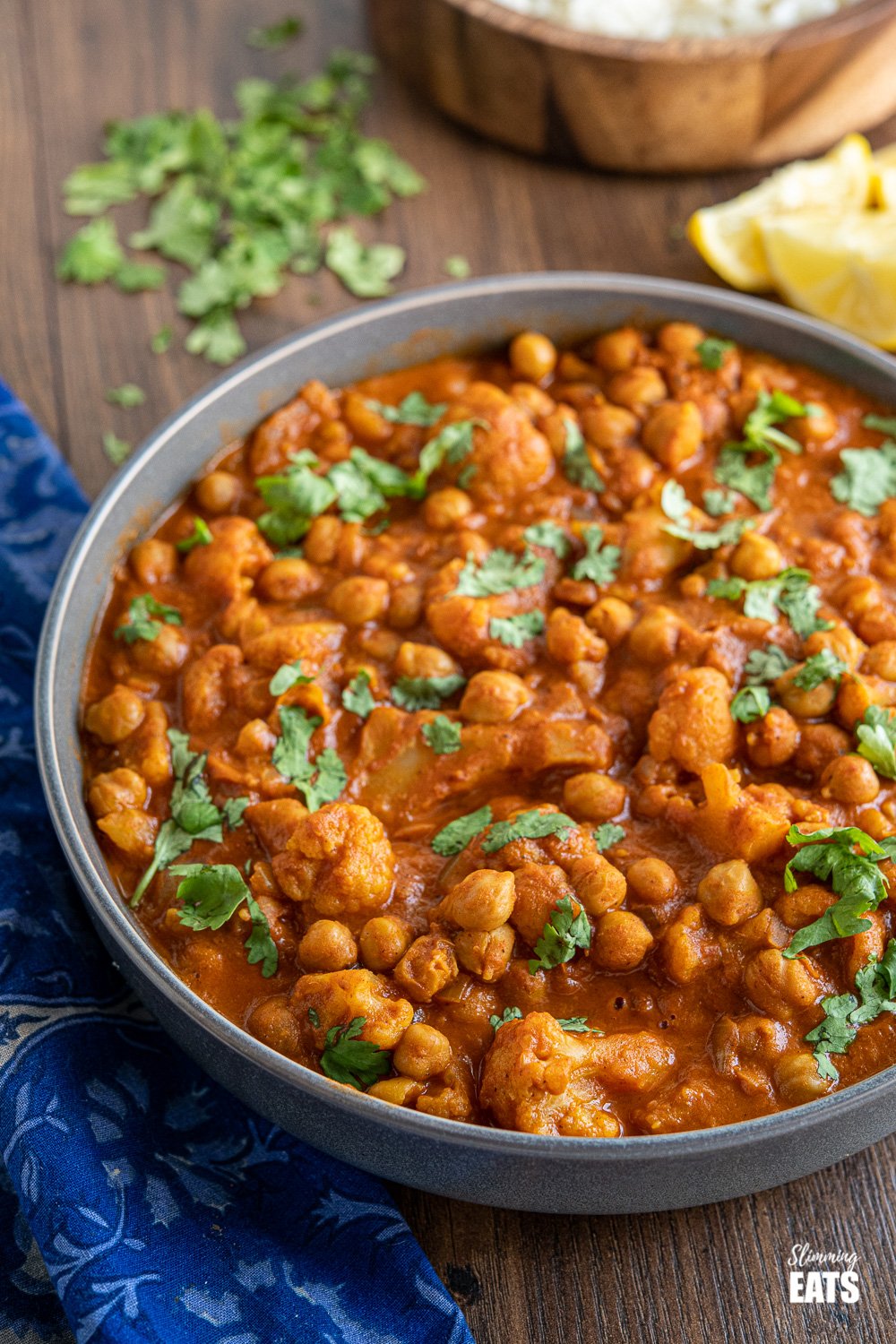 vegan tikka masala in grey bowl with rice in background in wooden bowl 