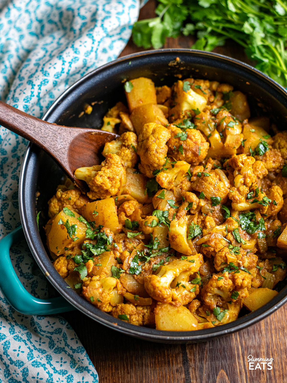 aloo gobi all cooked in a non stick double handled turquoise pan with wooden spoon 