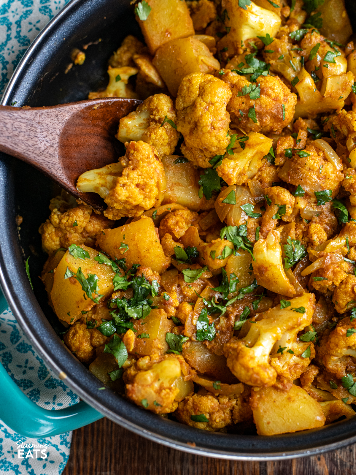 aloo gobi all cooked in a non stick double handled turquoise pan with wooden spoon 