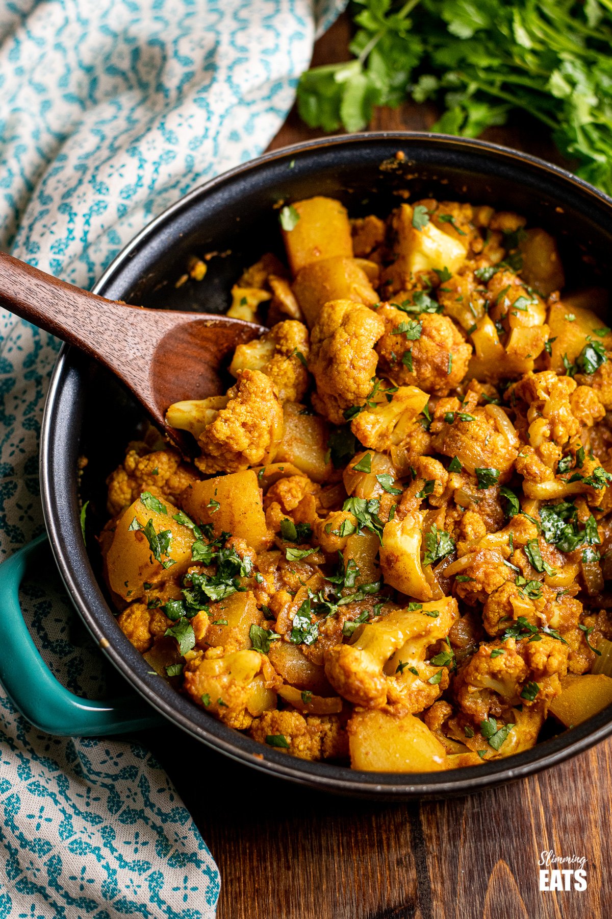 Aloo Gobi in a frying pan with wooden spoon