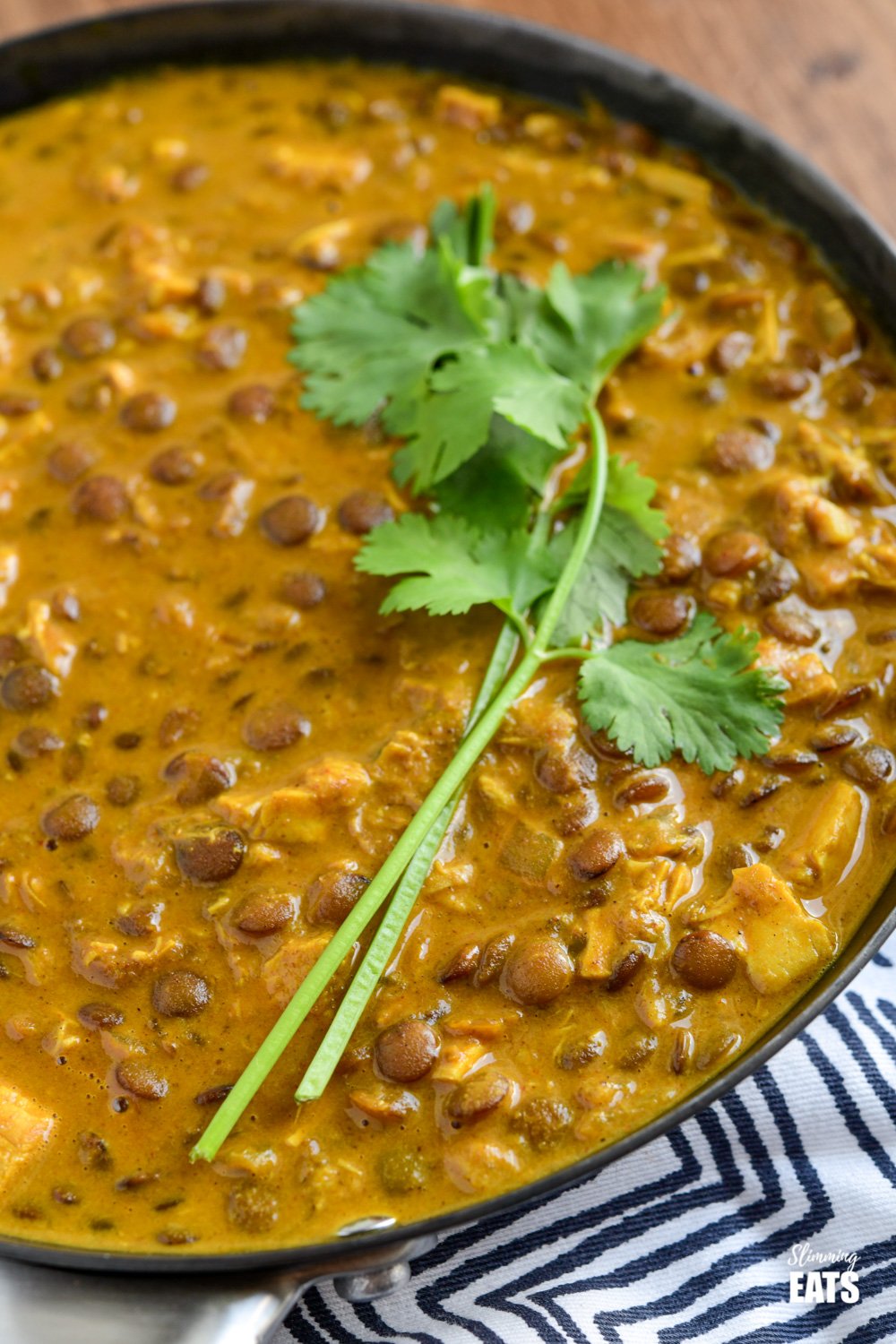 close up of coconut chicken and lentil curry in a frying pan topped with some fresh coriander