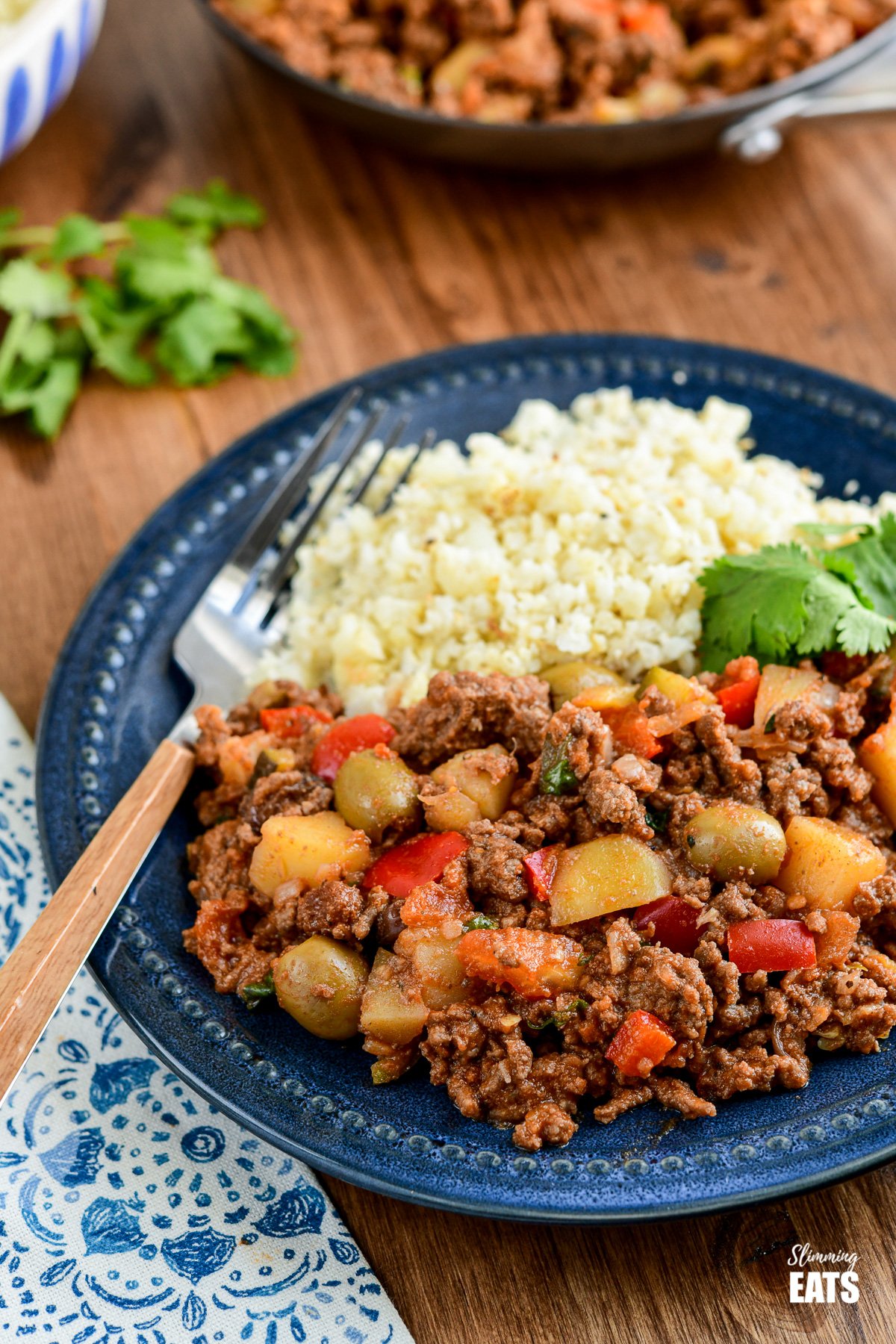Cuban Beef Picadillo - a delicious hearty ground beef Cuban inspired recipe with flavoursome spices, potatoes, vegetables, olives and sultanas. #Cuban #picadillo #olives #beef #slimmingeats #weightwatchers #glutenfree #dairyfree Cuban Beef Picadillo on dark blue plate with cauliflower rice