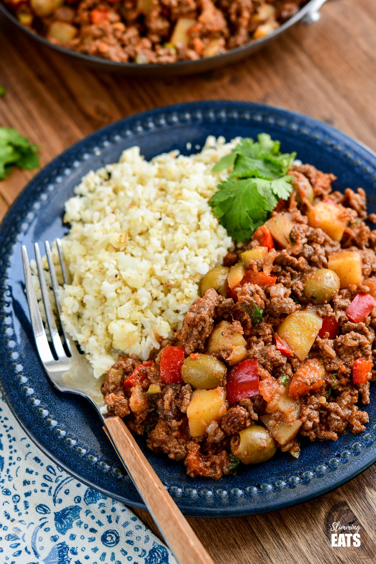 Cuban Beef Picadillo - a delicious hearty ground beef Cuban inspired recipe with flavoursome spices, potatoes, vegetables, olives and sultanas. #Cuban #picadillo #olives #beef #slimmingeats #weightwatchers #glutenfree #dairyfree Cuban Picadillo beef on dark blue plate with cauliflower rice and cilantro