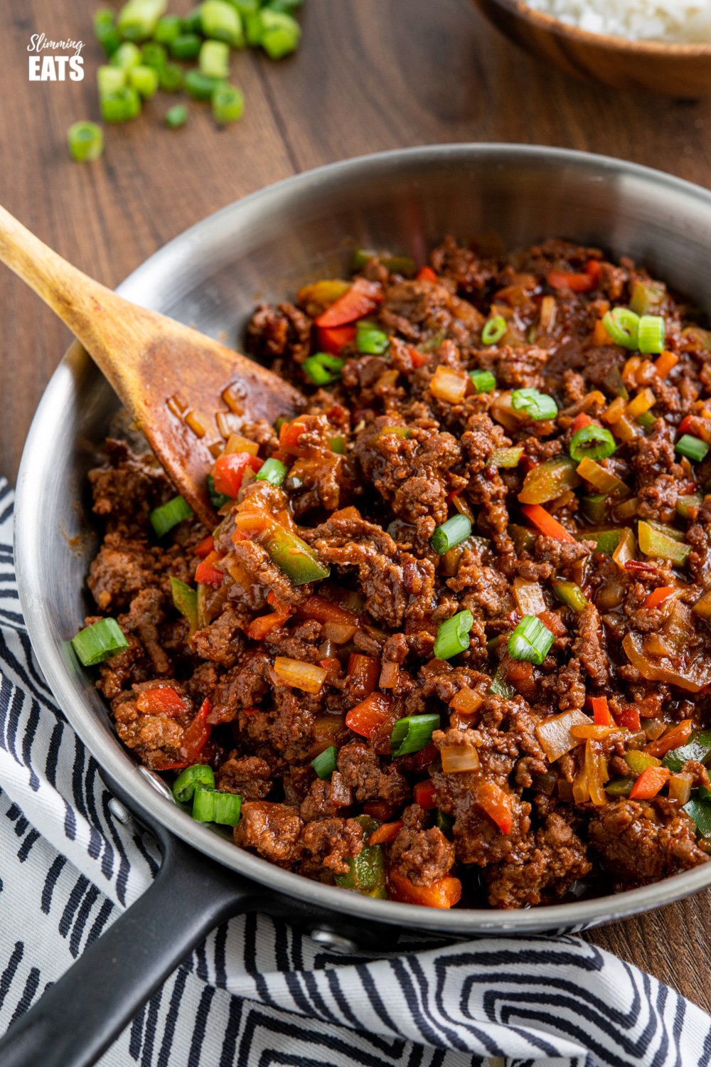 easy asian ground beef in frying pan with wooden spoon, scattered spring onions and black and white napkin