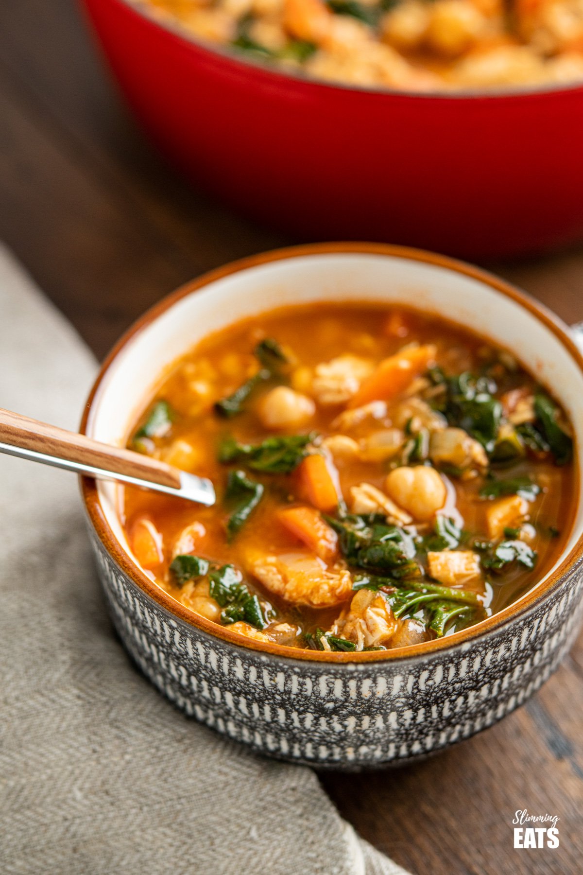 chicken chickpea spinach soup in cup with spoon, red cast iron pot in background