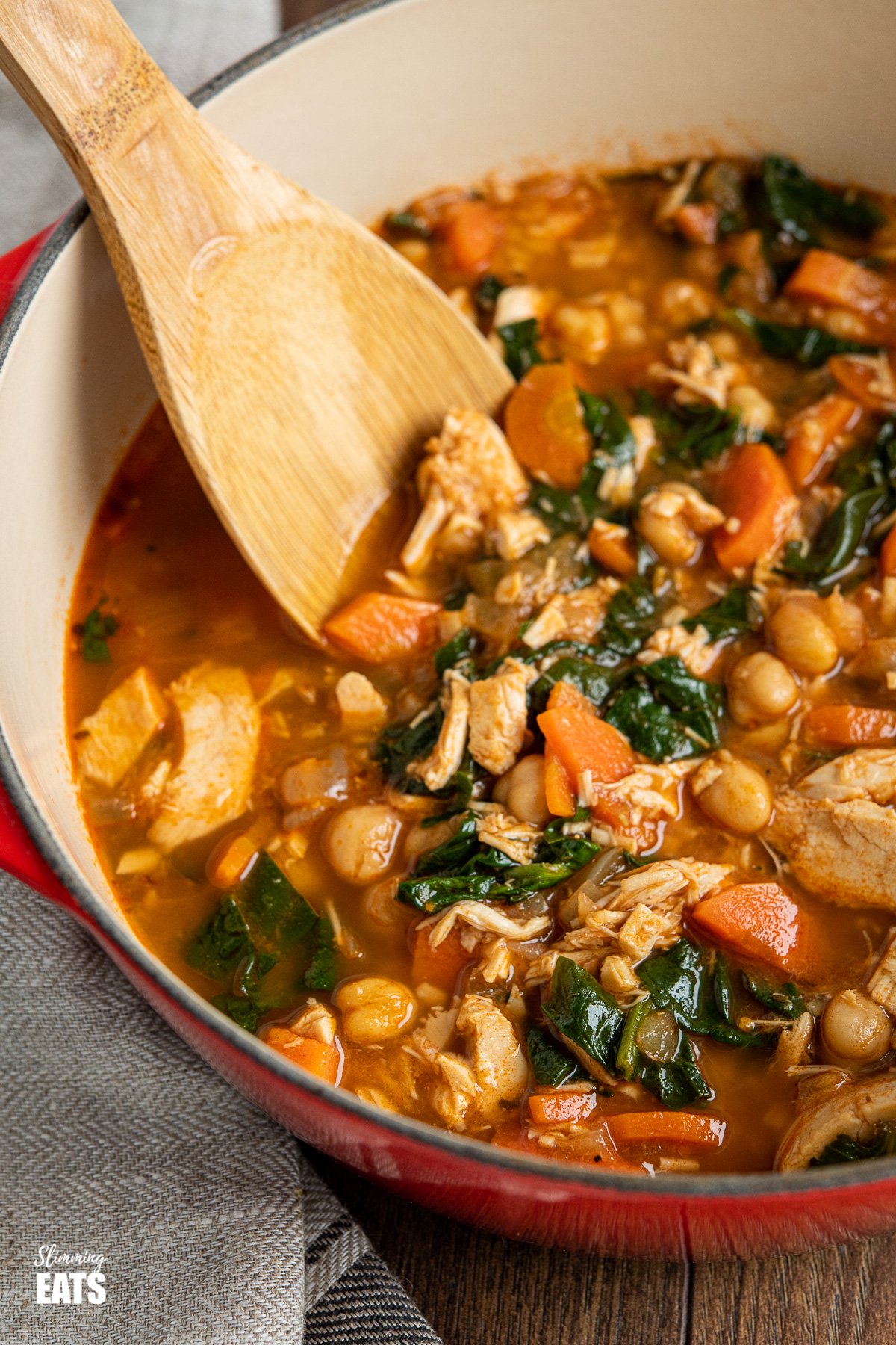  close up of chicken chickpea spinach soup in red cast iron pot with wooden spoon