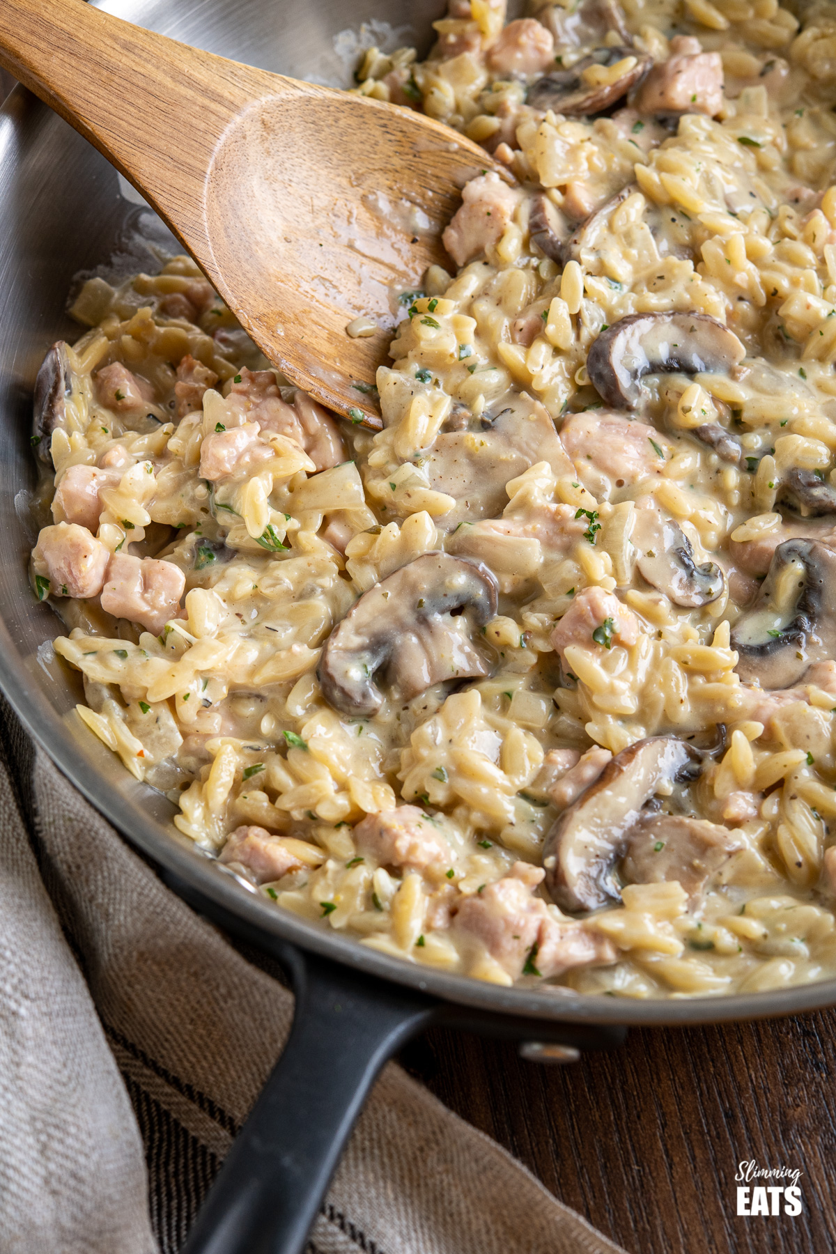 close up of creamy ham and mushroom orzo with wooden spoon