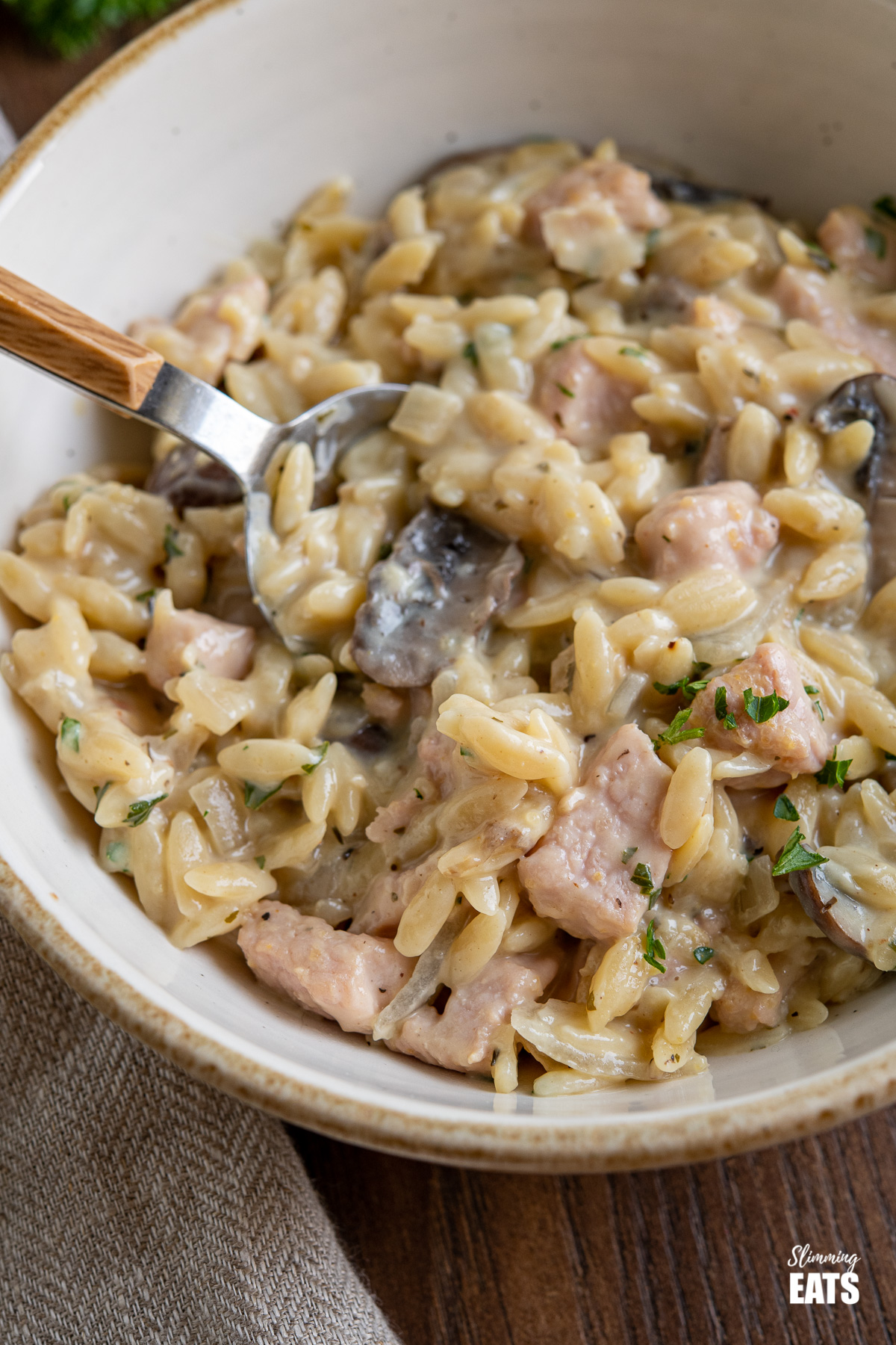 close up of creamy ham and mushroom orzo in bowl with spoon