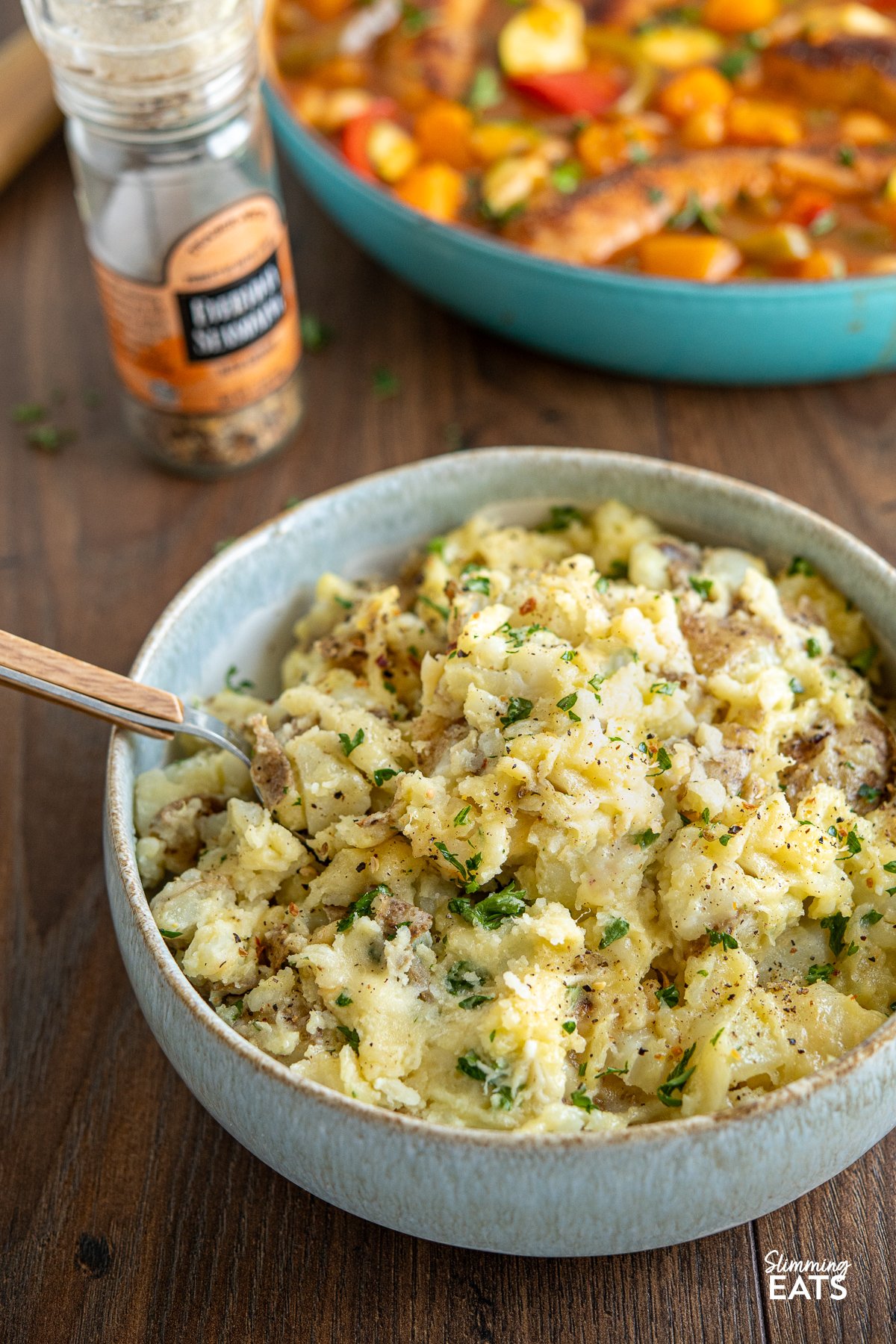 Rustic Parmesan Garlic Mashed Potatoes served in a pale blue and white bowl, accompanied by a spoon, with a tantalizing casserole in the background.