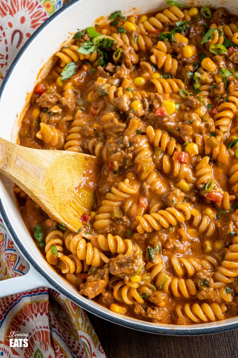 One Pot Taco Beef Pasta - an easy yummy recipe that is cooked all in one pan. Cheesy spicy taco flavoured deliciousness!! #slimmingeats #weightwatchers #onepot #beef #pasta #taco close up of taco beef pasta in skillet with wooden spoon