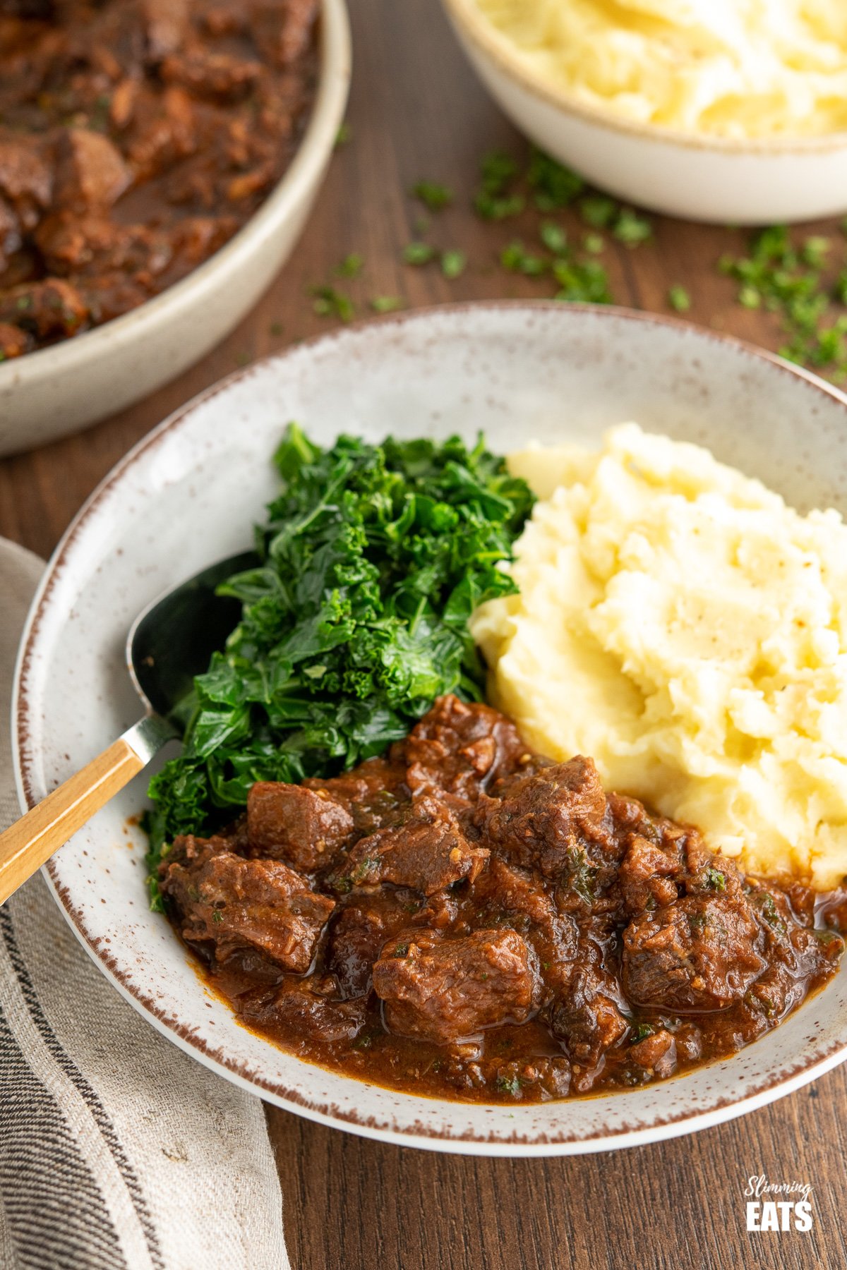beef and prune stew in beige bowl with mashed potatoes and kale