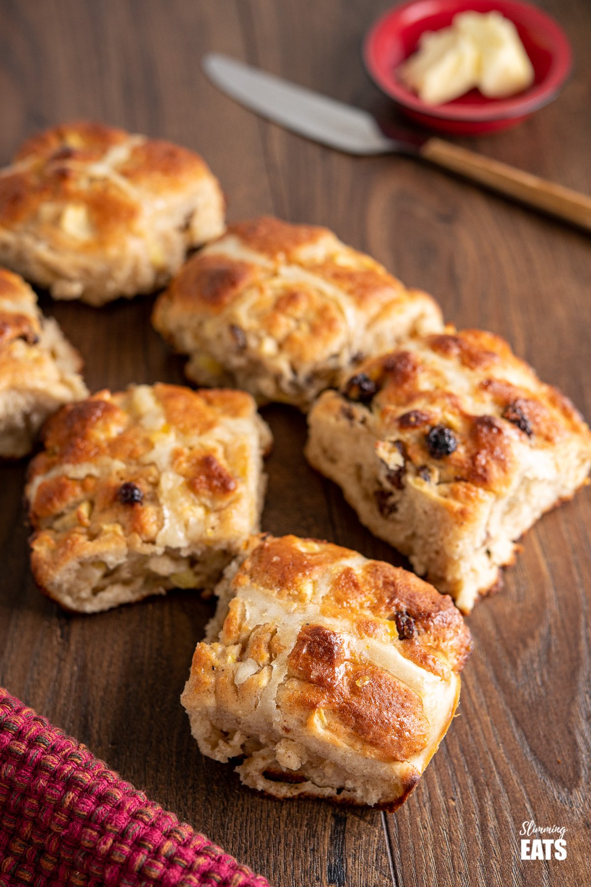 6 scattered hot cross buns on wooden table with butter and knife