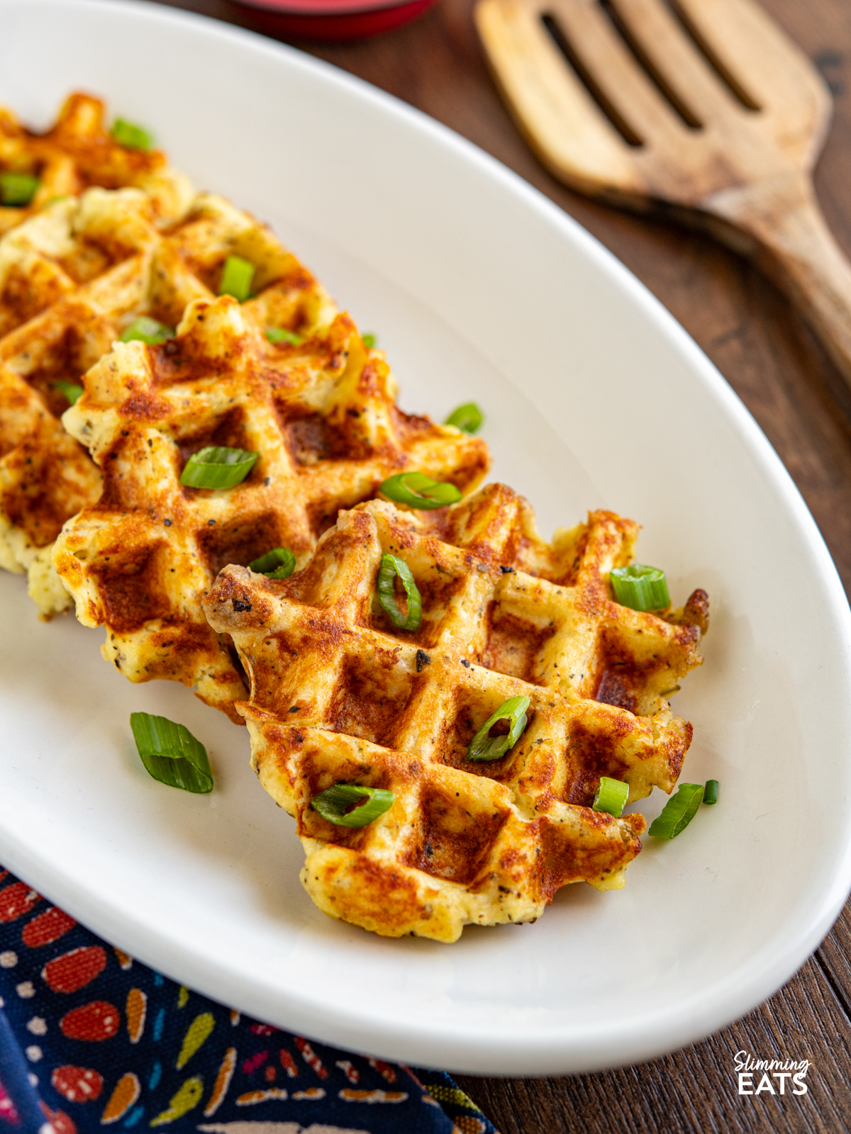 cooked potato waffles on a white oval plate garnished with chopped spring onion