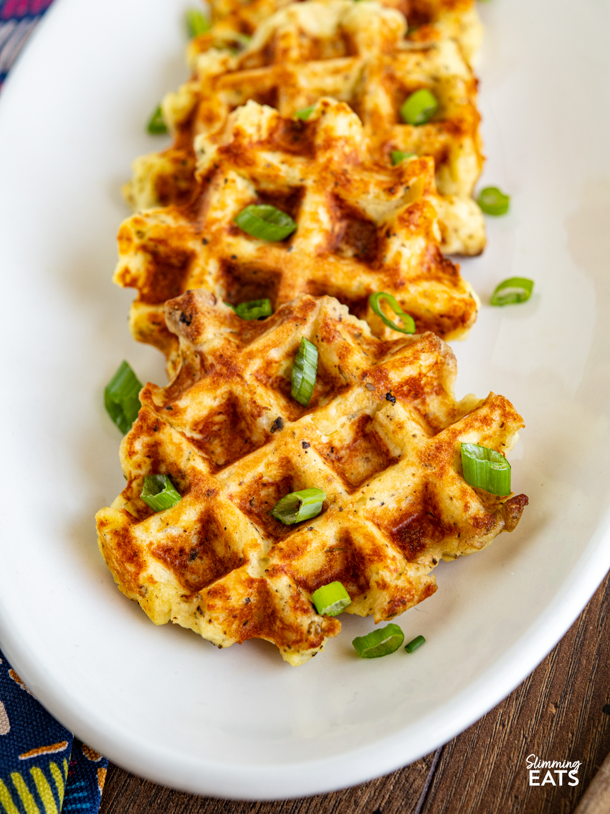 cooked potato waffles on a white oval plate garnished with chopped spring onion
