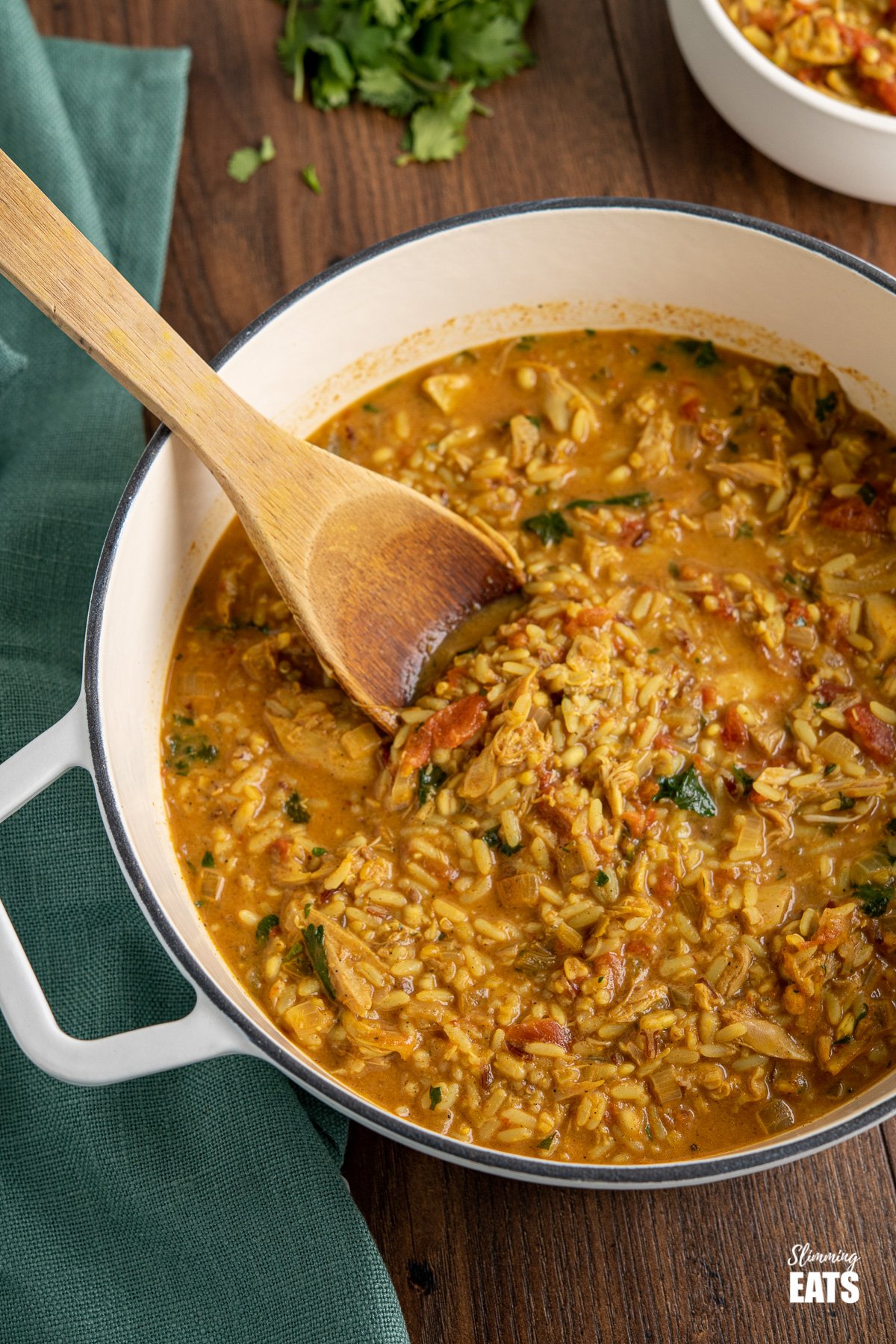 Coconut Chicken Rice Soup (from www.slimmingeats.com) - an easy to make filling bowl of soup that comes packed with flavour. You'll want to make this every week. #slimmingeats #weightwatchers #glutenfree #dairyfree #soup #chicken #rice Coconut Chicken Rice Soup in white cast iron pot with wooden spoon