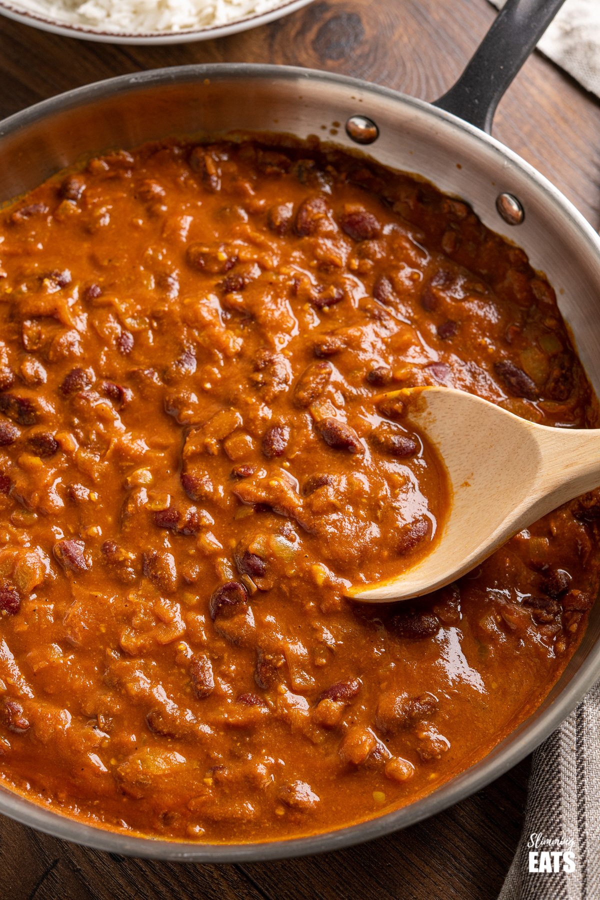 Kidney Bean Curry (Rajma) from www.slimmingeats.com - a delicious vegetarian curry made with Red Kidney Beans, onions, tomato (passata) and a blend of spices. #bean #curry #slimmingeats #weightwatchers #vegetarian #Indian close up of Kidney Bean Curry (Rajma) in stainless steel frying pan with wooden spoon