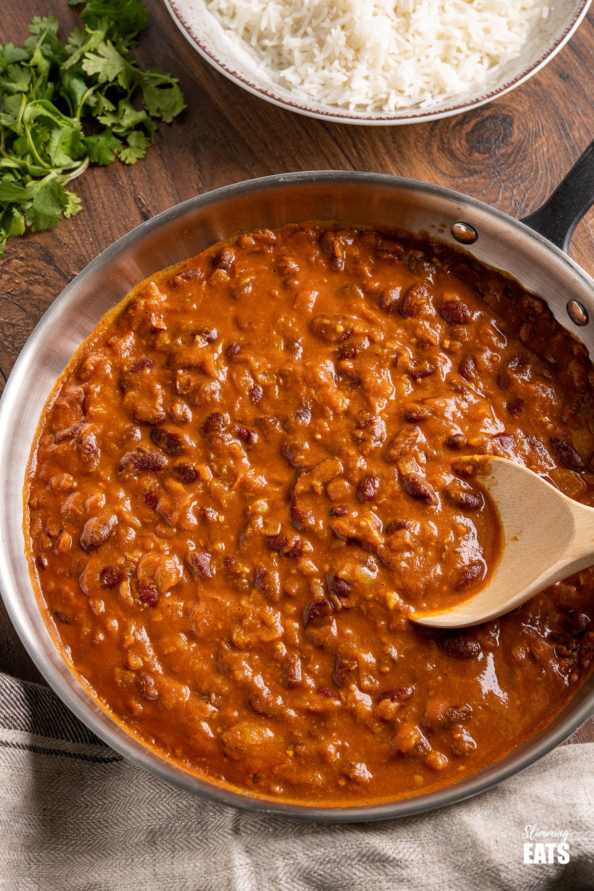 Kidney Bean Curry (Rajma) from www.slimmingeats.com - a delicious vegetarian curry made with Red Kidney Beans, onions, tomato (passata) and a blend of spices. #bean #curry #slimmingeats #weightwatchers #vegetarian #Indian Kidney Bean Curry in frying pan with bowl of rice and cilantro in background