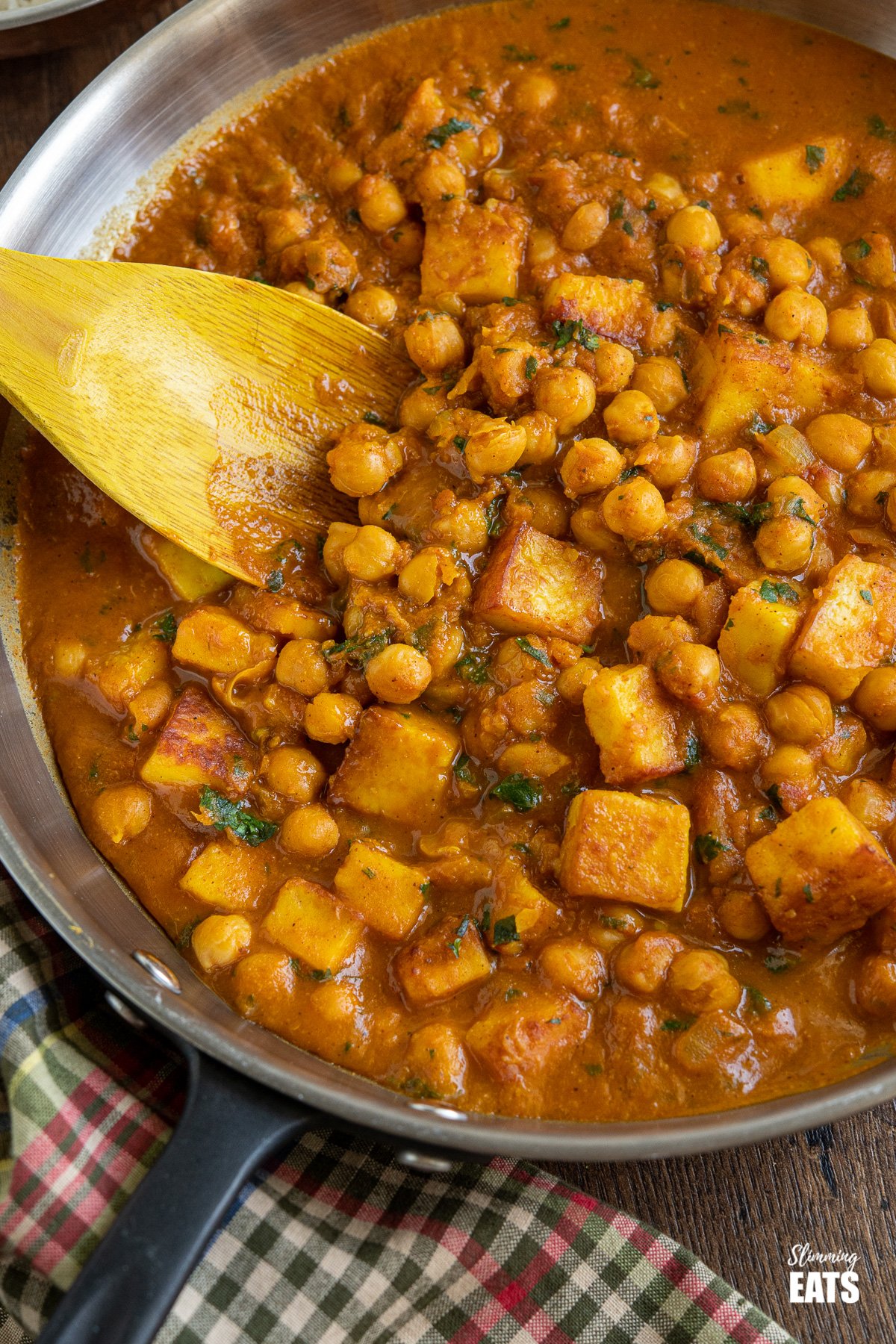 Chana Paneer (from www.slimmingeats.com)- A mixture of Chickpeas and cubes of Indian Paneer cheese with a blend of spices in a delicious flavoursome sauce. #paneer #Indian #chickpeas #vegetarian #slimmingeats #weightwatchers close up of Chana Paneer in black handled frying pan with wooden spoon